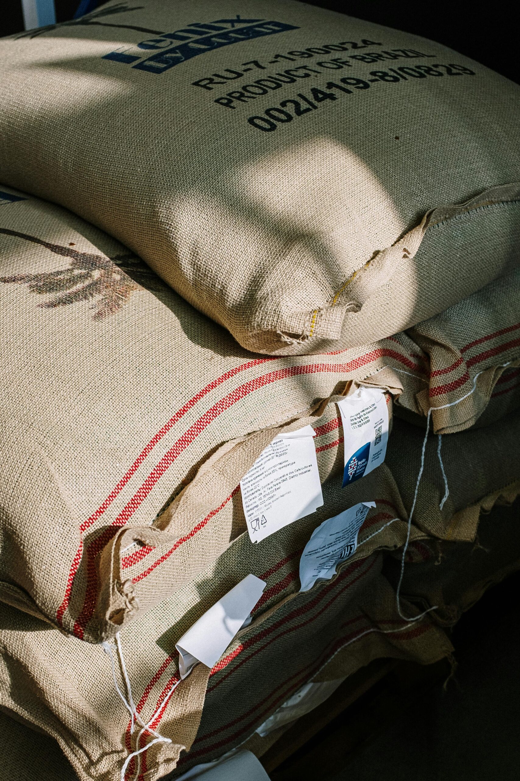 Stack of burlap sacks filled with organic coffee beans in a roastery, captured with natural light.